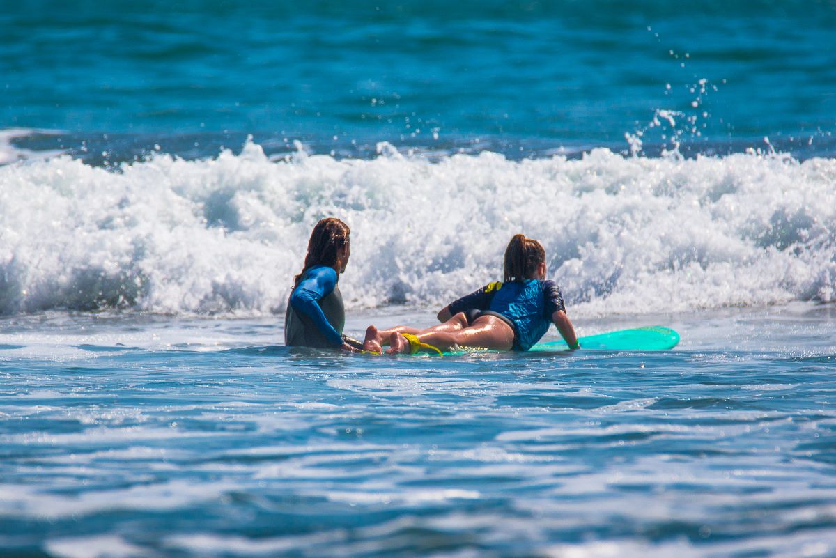 A female pushing another girl on a surf board in a Costa Rica surf lesson